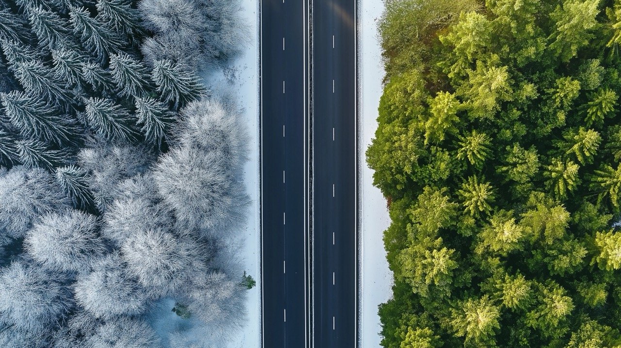 Aerial view of a highway road through the forest in summer and winter showcasing seasonal changes.